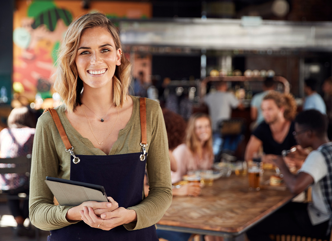 Restaurants and Hospitality Insurance in Maryland - Waitress Smiling with Restaurant of Restaurant Patrons Blurred in the Background