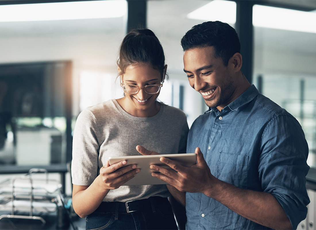 Review Our Agency - Portrait of Cheerful Young Male and Female Coworkers Looking at a Tablet While Standing in-the Office